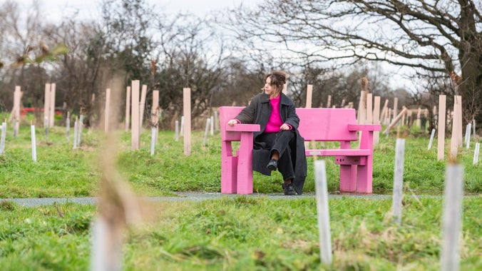 A woman sitting on a bright pink bench, deep in thought, in the Commemorative Woodland at Erddig.